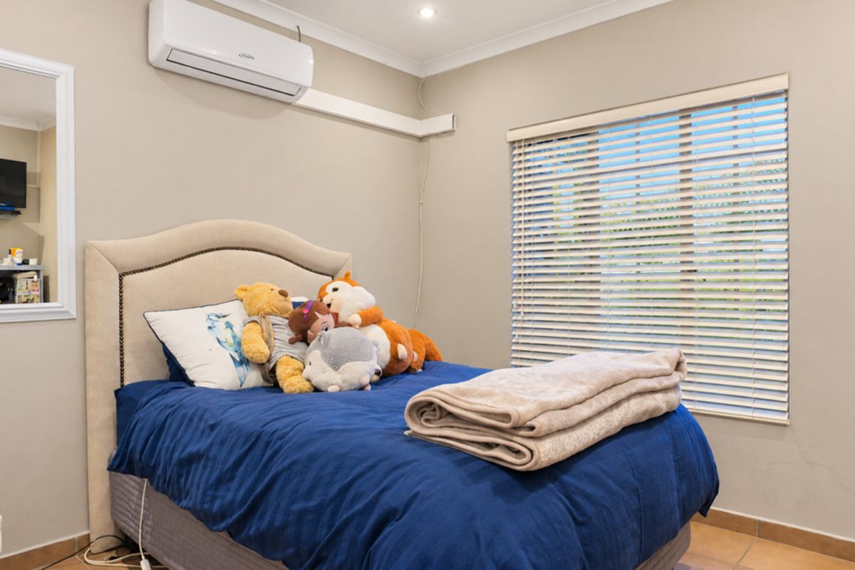 A well-maintained bedroom featuring tiled flooring, a wall-mounted split-system air conditioner, and venetian blinds for light control.