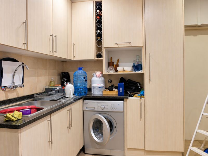 A functional laundry area featuring light wood-toned cabinetry, granite countertops, a stainless steel sink, and an integrated washing machine.