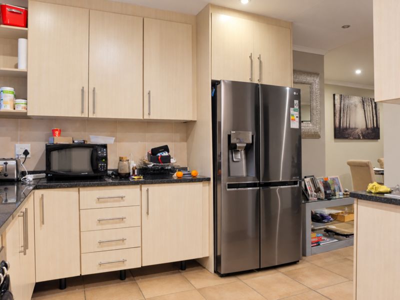A functional kitchen featuring light wood-finish cabinetry, dark granite countertops, tiled backsplash, and a large stainless steel refrigerator with integrated water dispenser.