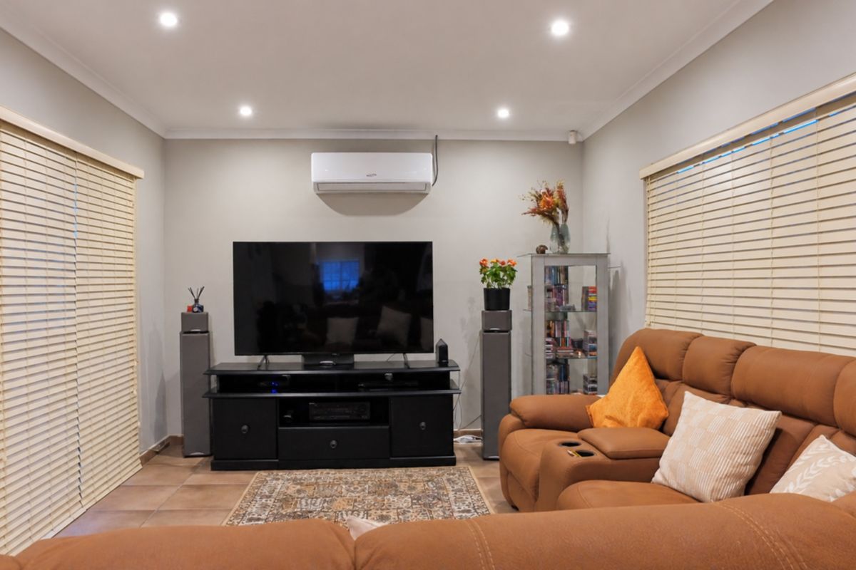 A well-maintained living room featuring tiled flooring, recessed downlighting, and a wall-mounted split-system air conditioner, complemented by dual venetian blinds.