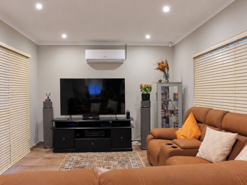 A well-maintained living room featuring tiled flooring, recessed downlighting, and a wall-mounted split-system air conditioner, complemented by dual venetian blinds.