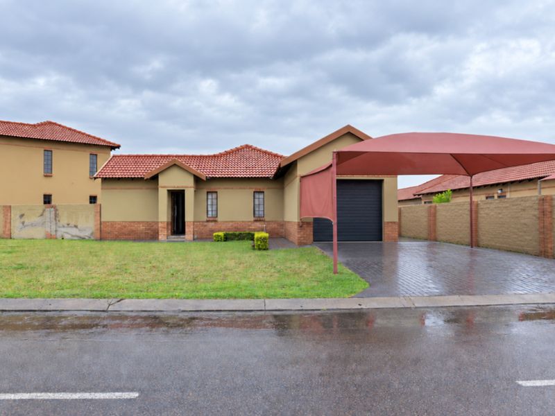 Front elevation of a single-story house featuring a tiled roof, brick accents, paved driveway with a shade sail carport, and a secure garage.