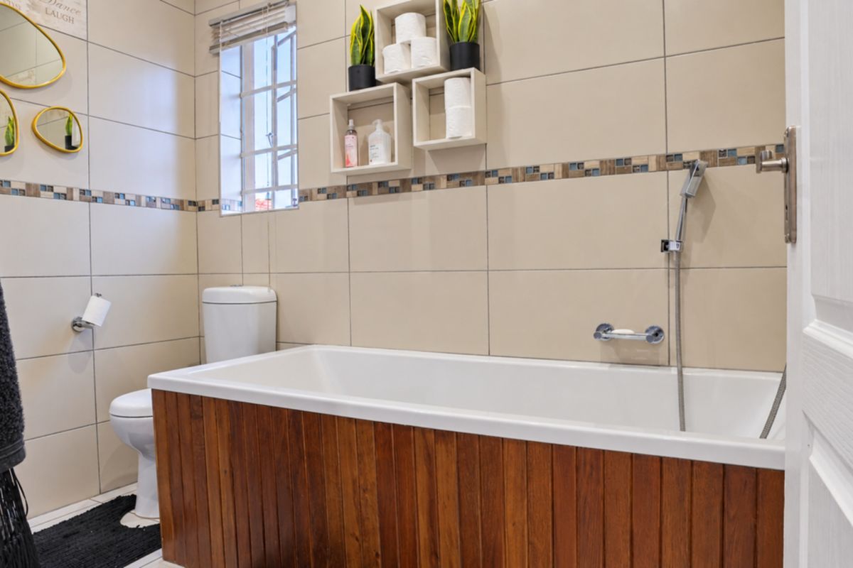 A well-maintained bathroom featuring a bathtub with a wooden panel finish, a toilet, and neutral wall tiling with a decorative mosaic border.