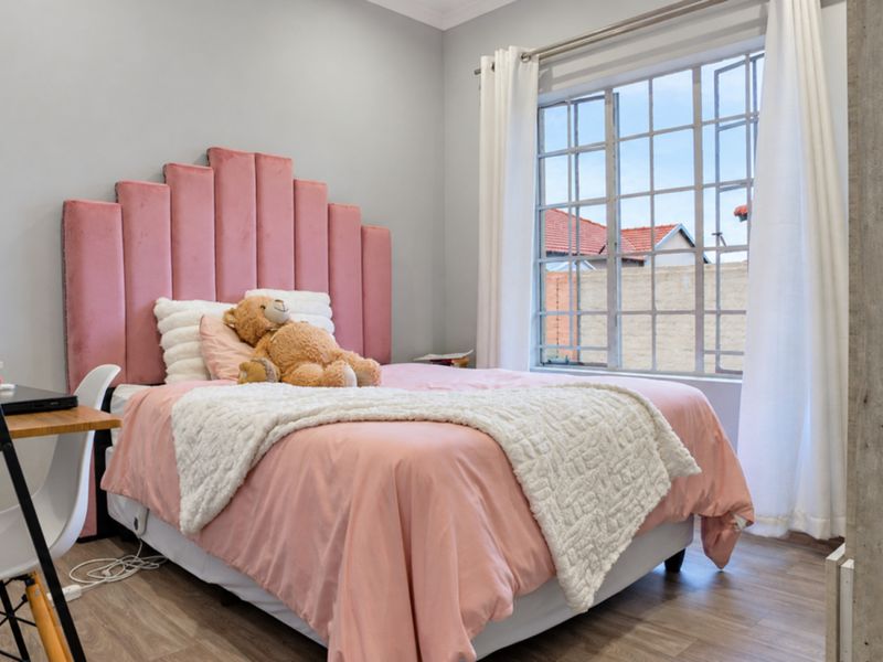 A well-lit bedroom featuring laminate flooring and a large steel-framed window, providing a bright and comfortable living space.