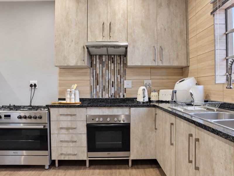 Modern kitchen featuring light wood-finish cabinetry, granite countertops, stainless steel appliances, and a decorative mosaic tile backsplash.