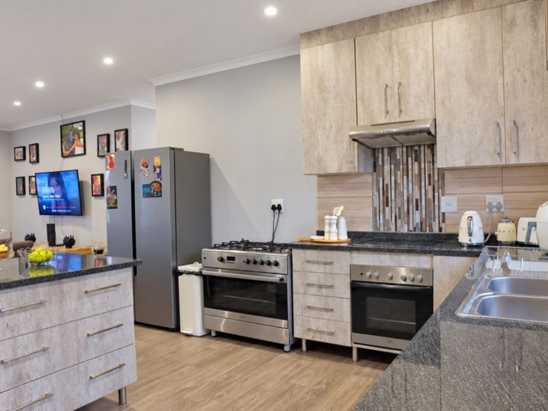 Modern open-plan kitchen featuring granite countertops, light wood-finish cabinetry, a gas stove, and integrated appliances, flowing into the adjacent living area.