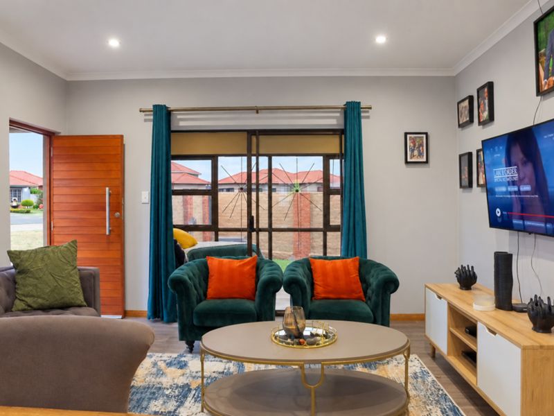 A well-maintained living room featuring laminate flooring, recessed downlights, and direct access to the exterior through a sliding glass door and wooden entrance door.