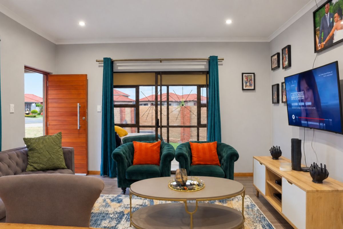 A well-maintained living room featuring laminate flooring, recessed downlights, and direct access to the exterior through a sliding glass door and wooden entrance door.