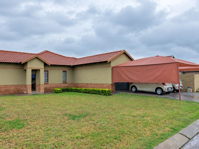 Front view of a single-story house featuring a tiled roof, brick and plaster facade, and a covered carport area with a paved driveway.