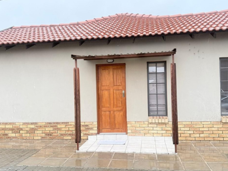 Front elevation of a single-story house featuring a tiled roof, brick base detailing, and a covered entrance porch with a wooden door.