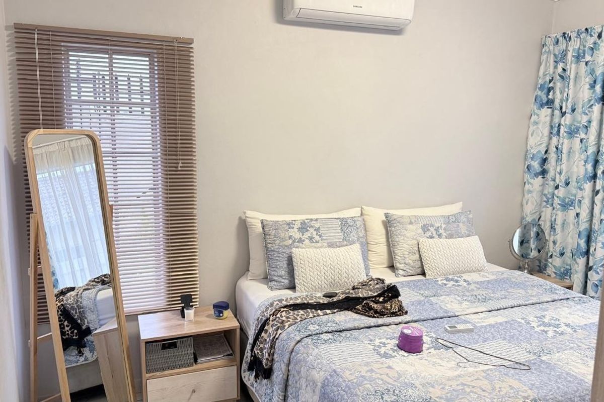 A well-maintained bedroom featuring a wall-mounted split-system air conditioner and venetian blinds, providing a comfortable and functional living space.