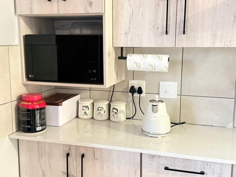 A modern kitchen area featuring light wood-grain cabinetry, stone countertops, a tiled backsplash, and a built-in microwave unit.
