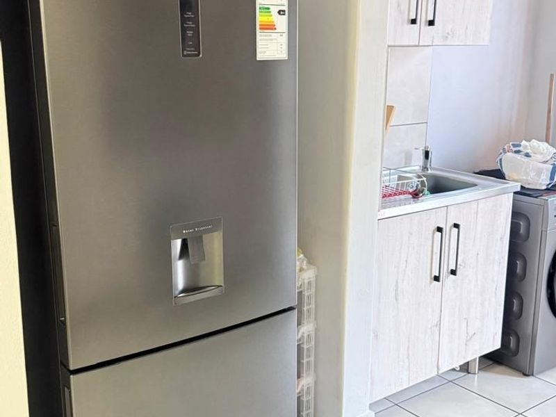 A functional laundry area featuring built-in cabinetry, a stainless steel sink, and clean tiled flooring.