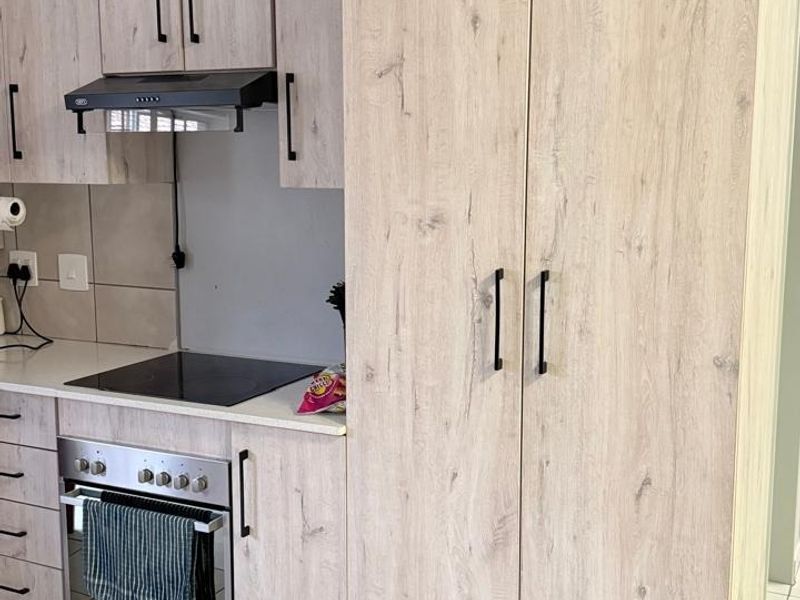 Modern kitchen featuring light wood-grain cabinetry, integrated electric hob, oven, and extractor fan with clean tiled flooring and backsplash.