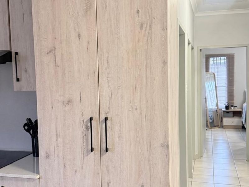 A modern kitchen featuring light wood-grain cabinetry, a built-in cooktop, and extractor fan, with tiled flooring leading into a hallway.