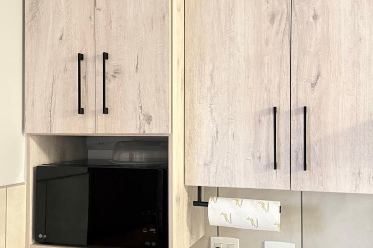 A modern kitchen section featuring light wood-grain cabinetry, stone countertops, a tiled backsplash, and a built-in microwave nook.