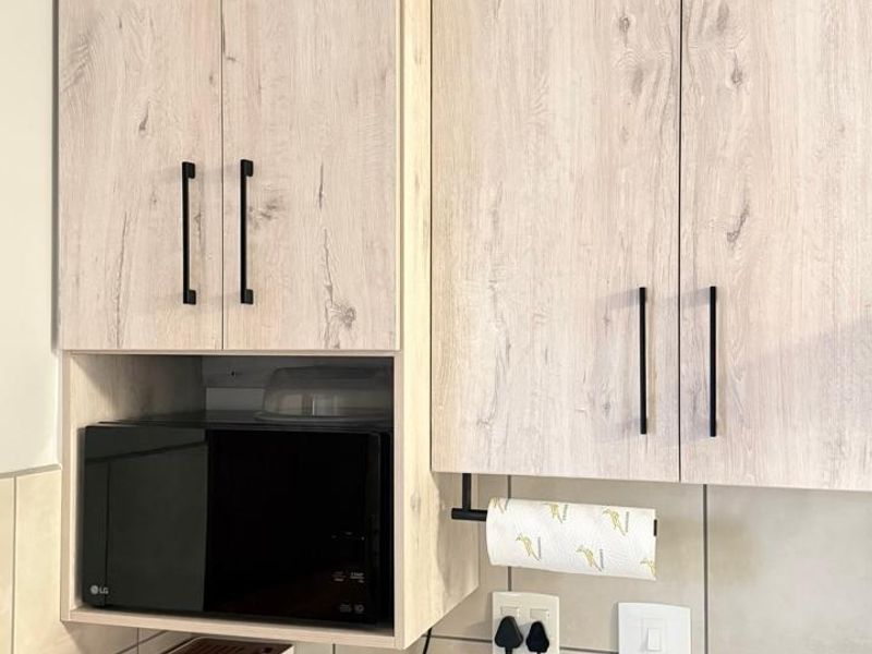A modern kitchen section featuring light wood-grain cabinetry, stone countertops, a tiled backsplash, and a built-in microwave nook.