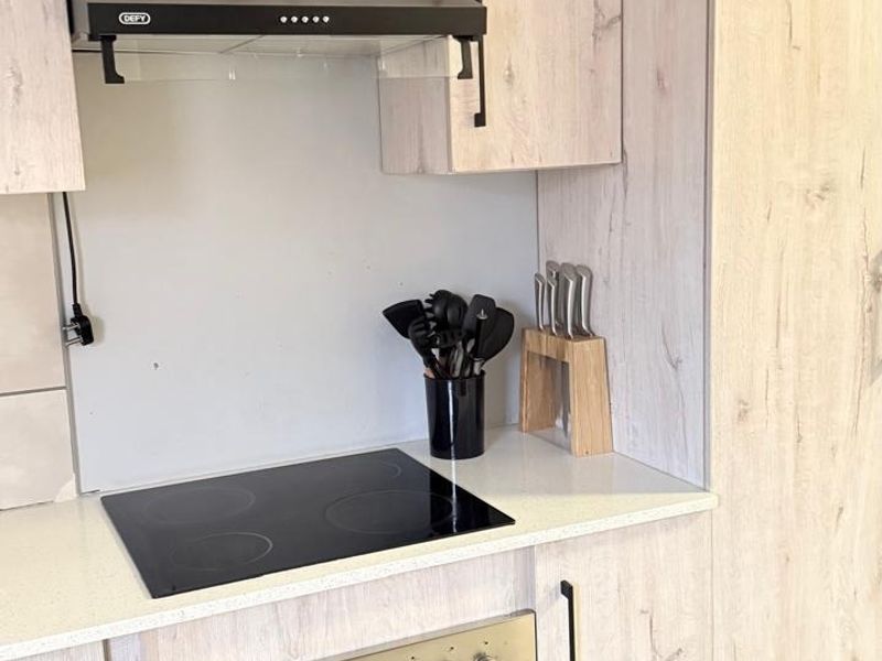 Modern kitchen featuring light wood-grain cabinetry, stone countertops, a built-in oven, and an electric hob with an extractor fan.