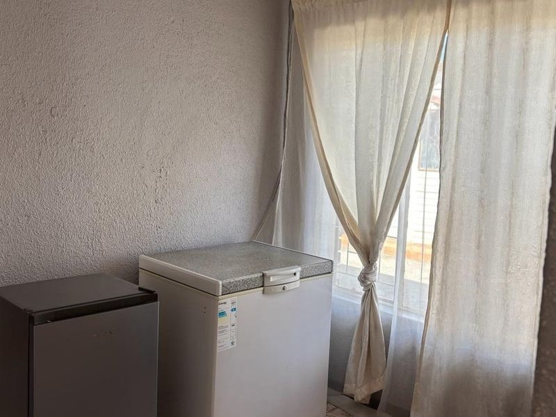 A functional utility or scullery area featuring textured walls and a window with curtains, suitable for storage or secondary kitchen tasks.