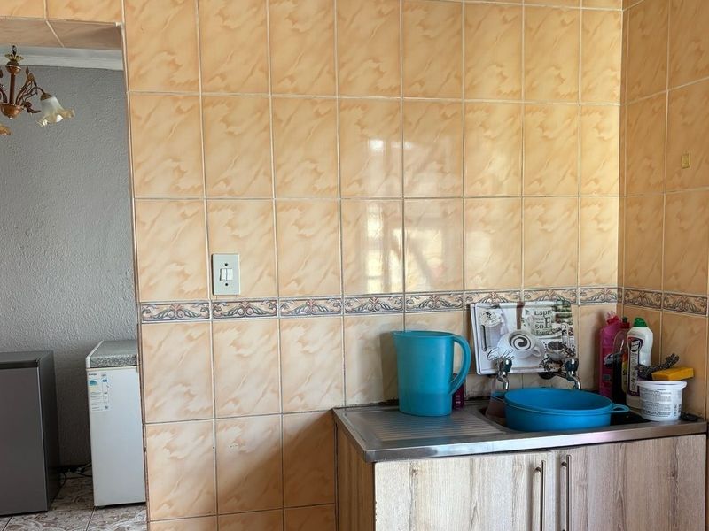 A functional scullery area featuring a stainless steel sink, tiled wall finishes, and built-in cabinetry, providing a practical space for food preparation and cleaning.