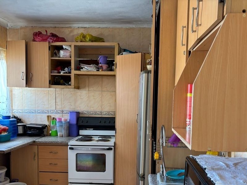 A functional kitchen featuring laminate cabinetry, tiled backsplash, and a freestanding electric stove, offering potential for modernization and cosmetic updates.