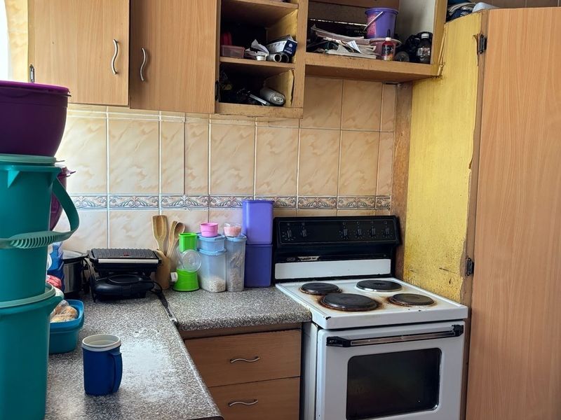 A compact kitchen featuring laminate cabinetry, tiled backsplash, and a freestanding electric stove, requiring cosmetic updates to improve its overall condition and functionality.