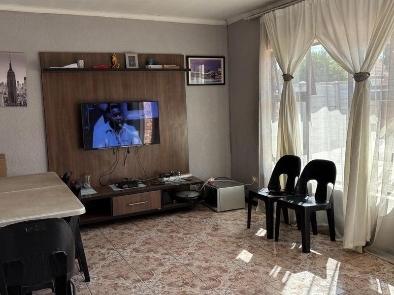 A living room featuring tiled flooring, a built-in media unit, and a sliding glass door providing natural light.
