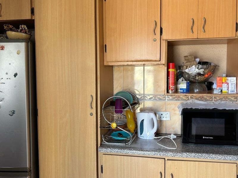 A dated kitchen featuring laminate cabinetry, tiled backsplash, and a built-in microwave area, offering potential for a modern renovation.