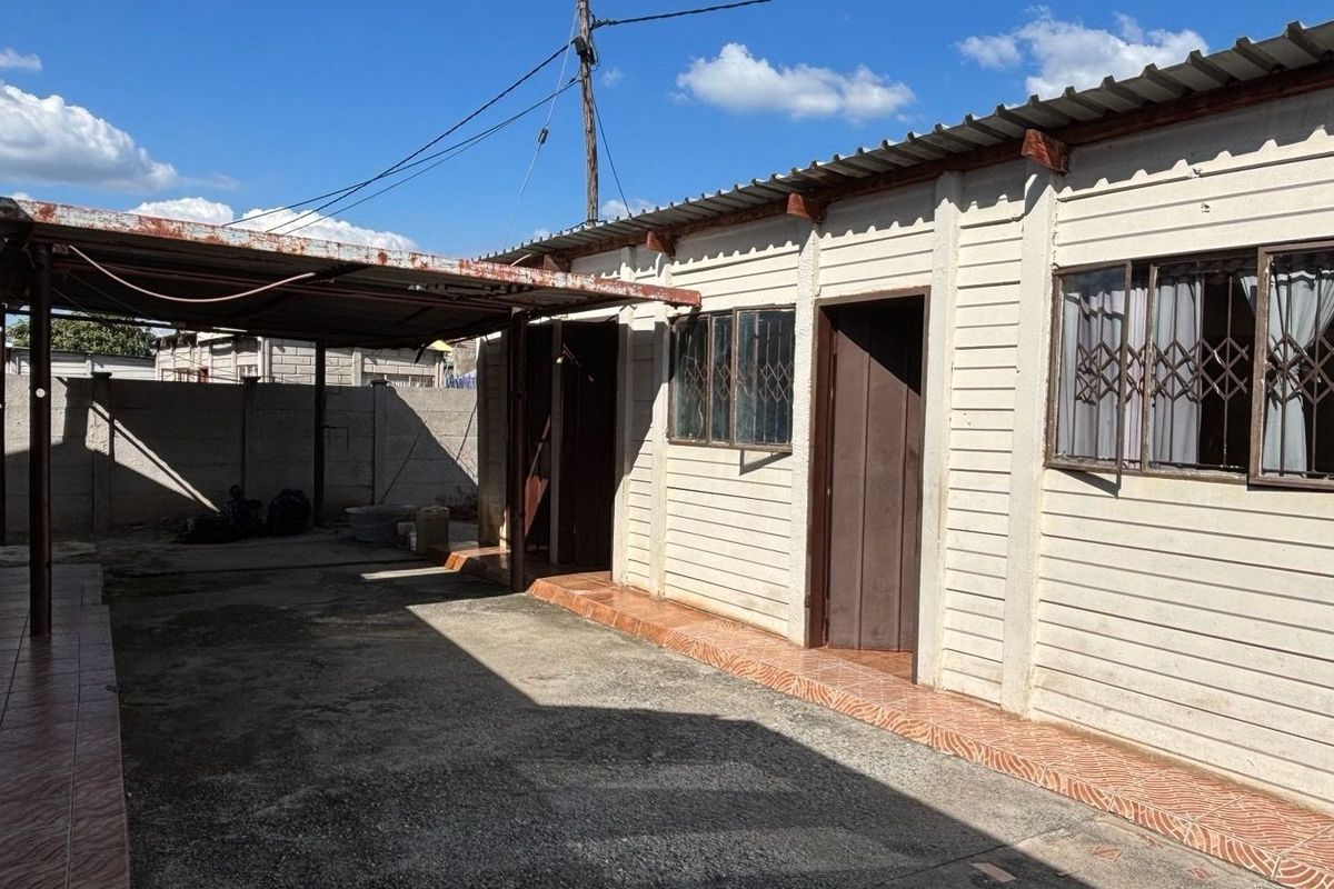 Rear exterior view of the property featuring a concrete driveway, a covered carport area, and a perimeter wall with security window bars.