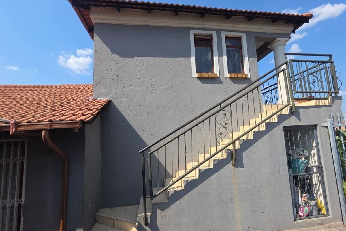 Exterior view of a two-story house section featuring an external staircase with wrought iron railings and terracotta roof tiles.