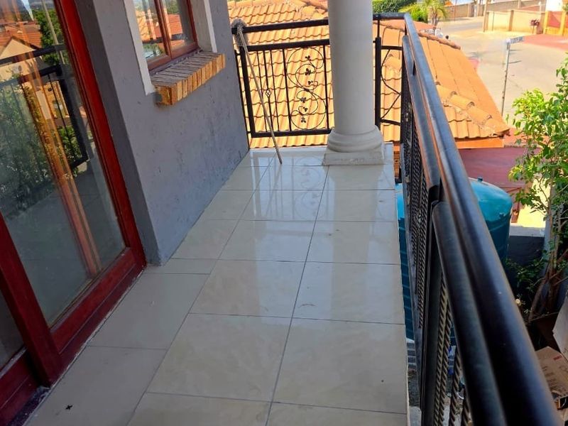 A tiled balcony featuring a wrought iron balustrade and a decorative column, providing an elevated outdoor space with views of the surrounding neighborhood.
