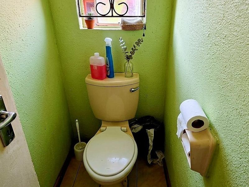 A compact guest toilet featuring a standard porcelain toilet, tiled flooring, and a small window with security bars.