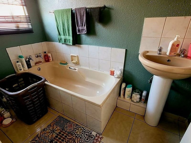 A functional bathroom featuring a standard bathtub, pedestal basin, and tiled finishes, offering potential for modernization and cosmetic updates.
