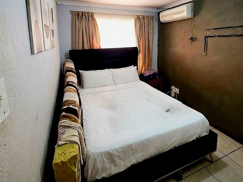 A compact bedroom featuring tiled flooring, an installed air conditioning unit, and neutral wall finishes, offering a functional space for rest.