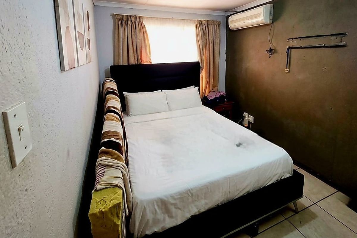 A compact bedroom featuring tiled flooring, an installed air conditioning unit, and neutral wall finishes, offering a functional space for rest.