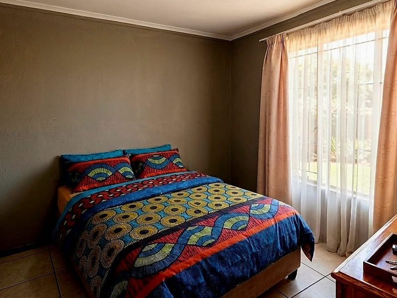 A standard bedroom featuring tiled flooring and large windows with curtain rails, providing natural light and a neutral wall finish.