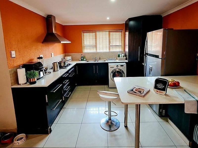 A functional kitchen featuring dark cabinetry, a breakfast bar, tiled flooring, and a stainless steel extractor fan with a vibrant orange accent wall.