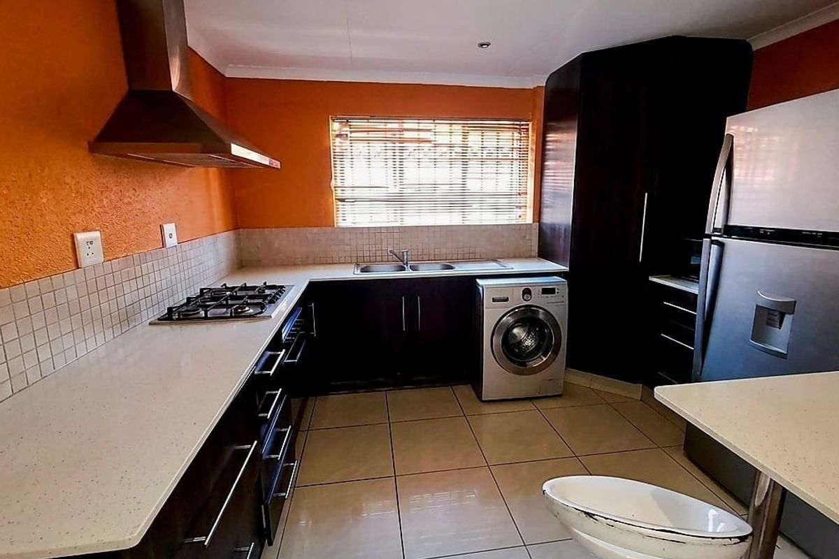 Functional kitchen featuring dark cabinetry, stone countertops, gas hob, stainless steel extractor fan, and tiled flooring with integrated laundry appliance space.