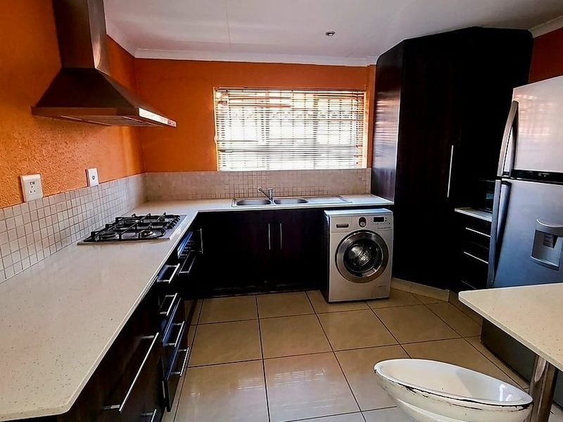 Functional kitchen featuring dark cabinetry, stone countertops, gas hob, stainless steel extractor fan, and tiled flooring with integrated laundry appliance space.