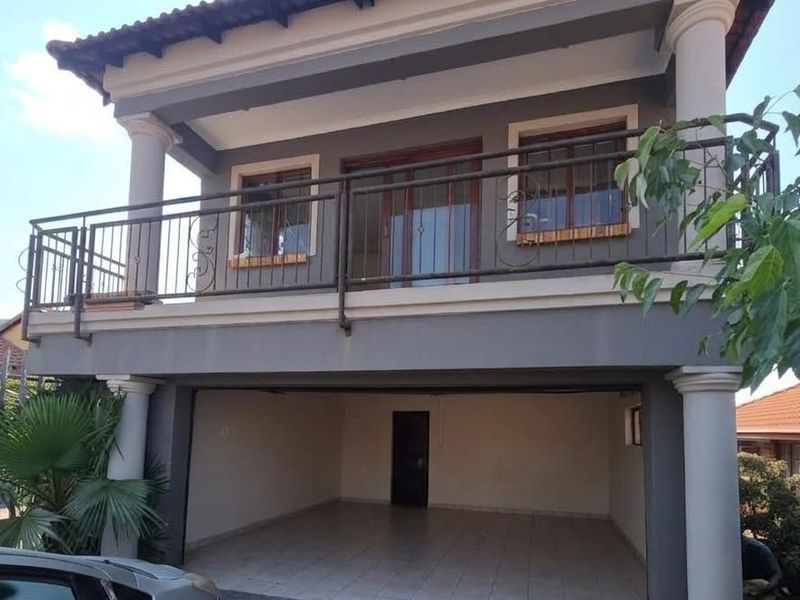 Front elevation of a two-story house featuring a covered ground-level garage and an upper-level balcony with wrought iron railings.