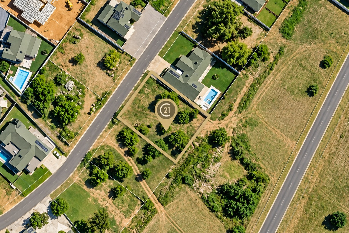 An aerial view of a vacant residential plot featuring established trees, situated within a developed suburban estate.