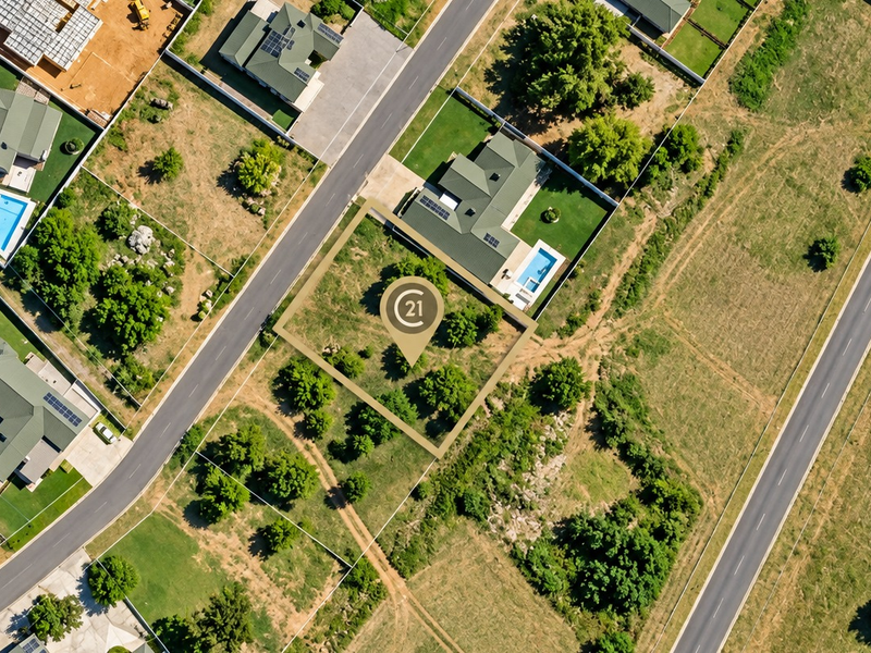 An aerial view of a vacant residential plot featuring established trees, situated within a developed suburban estate.