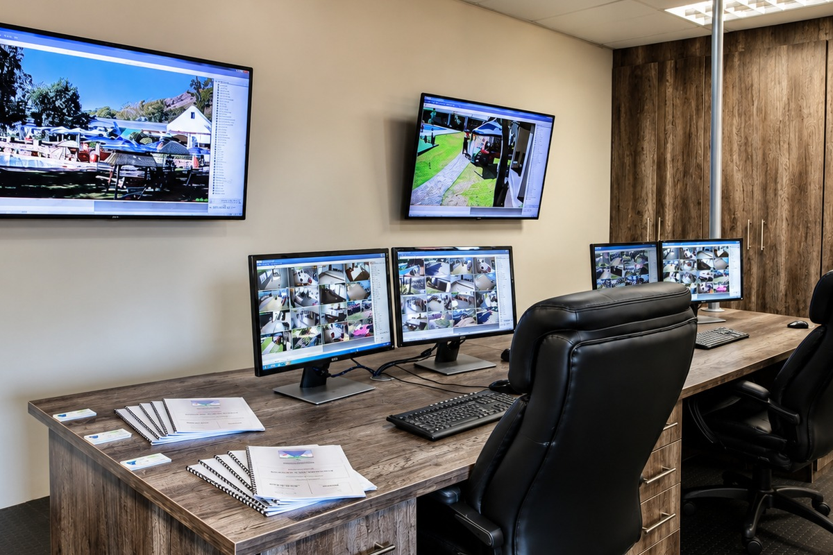 A professional security monitoring room featuring built-in cabinetry, integrated desk space, and multiple wall-mounted and desktop surveillance monitors.
