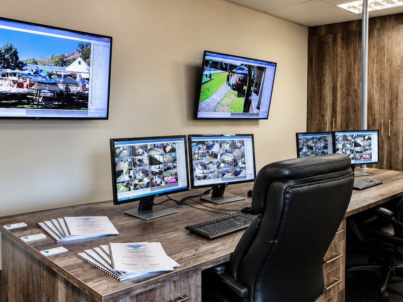 A professional security monitoring room featuring built-in cabinetry, integrated desk space, and multiple wall-mounted and desktop surveillance monitors.
