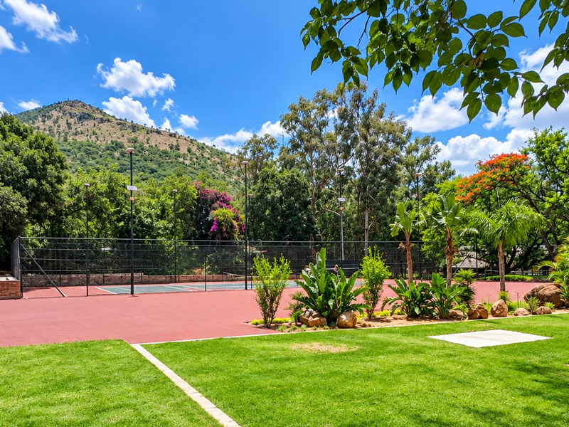 A well-maintained private tennis court set within a lush, landscaped garden with mountain views and integrated floodlighting.