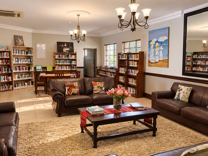 Spacious living area featuring built-in bookshelves, elegant chandeliers, crown molding, and large wall mirrors, creating a comfortable and well-maintained communal space.