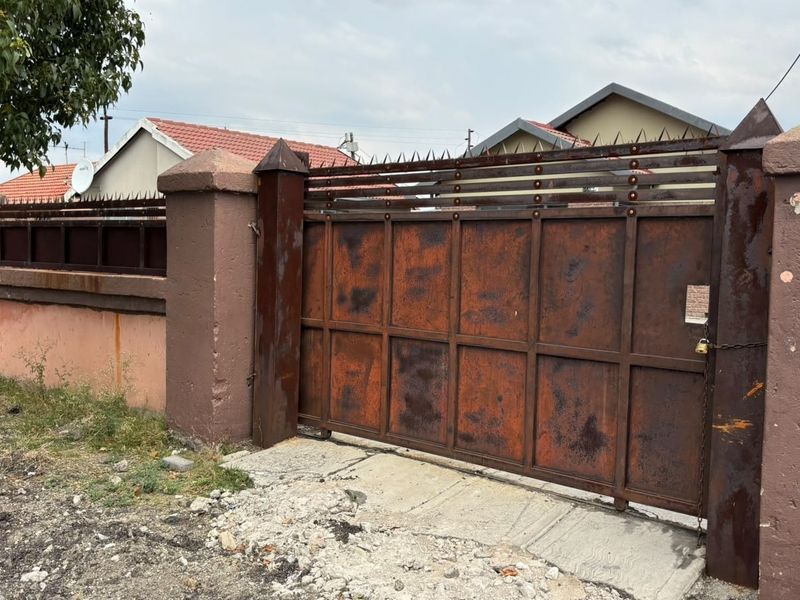 Front view of the property featuring a metal sliding gate and perimeter wall showing significant signs of rust and weathering.