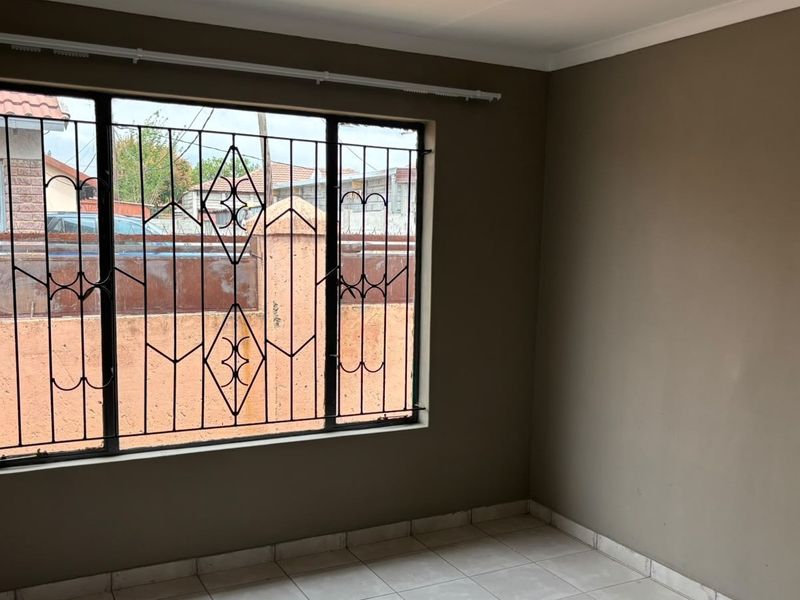 A clean, empty bedroom featuring neutral wall paint, tiled flooring, and security bars on the window.