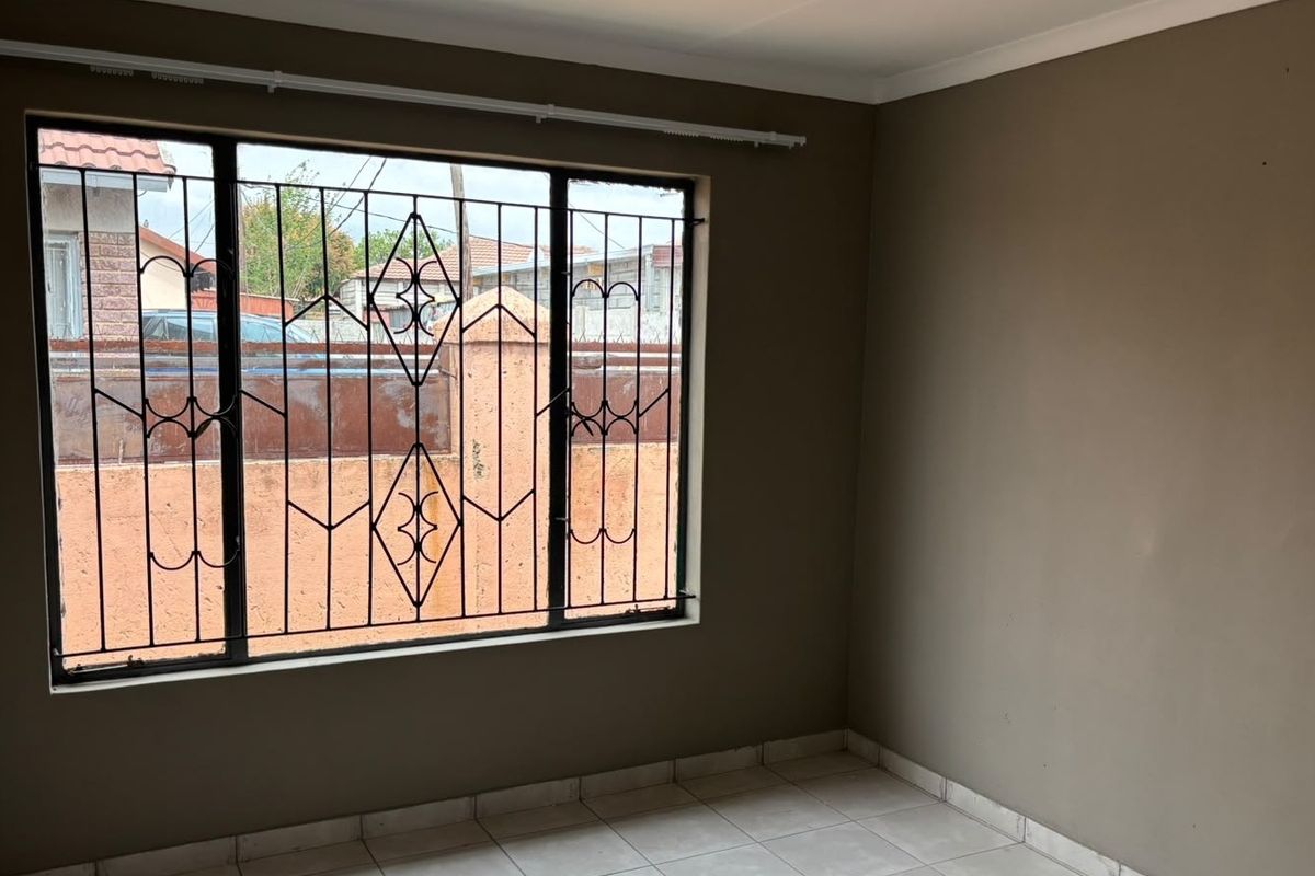 A clean, empty bedroom featuring neutral wall paint, tiled flooring, and security bars on the window.