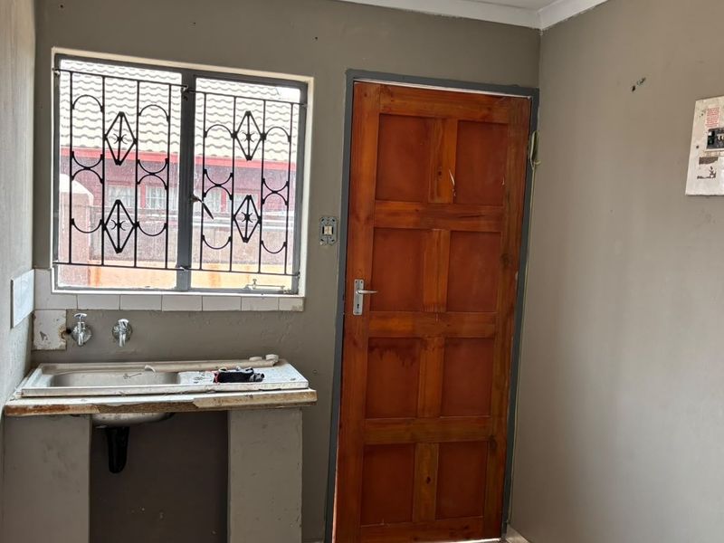 A basic utility or scullery area featuring a stainless steel sink, timber door, and exposed electrical distribution board, requiring cosmetic updates and repairs.